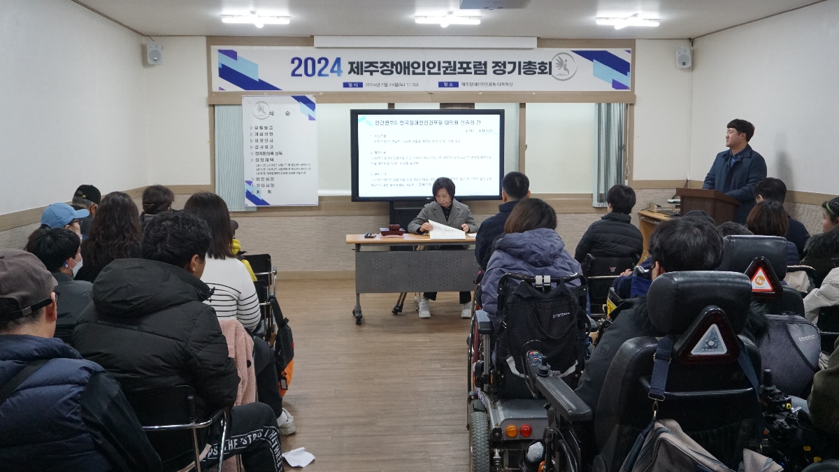 정기총회 장면, 많은사람들이 강당에 모여 최희순 대표님이 의안 채택하는 모습을 보고 있다.